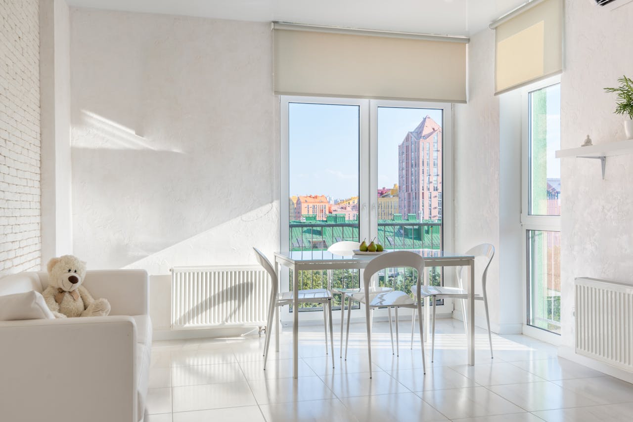 Sunlit modern interior with white decor and city view from large windows.
